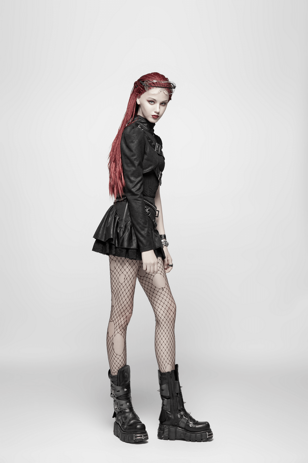 Edgy model in a one shoulder faux leather punk jacket with buckles and fishnet tights, showcasing gothic fashion.