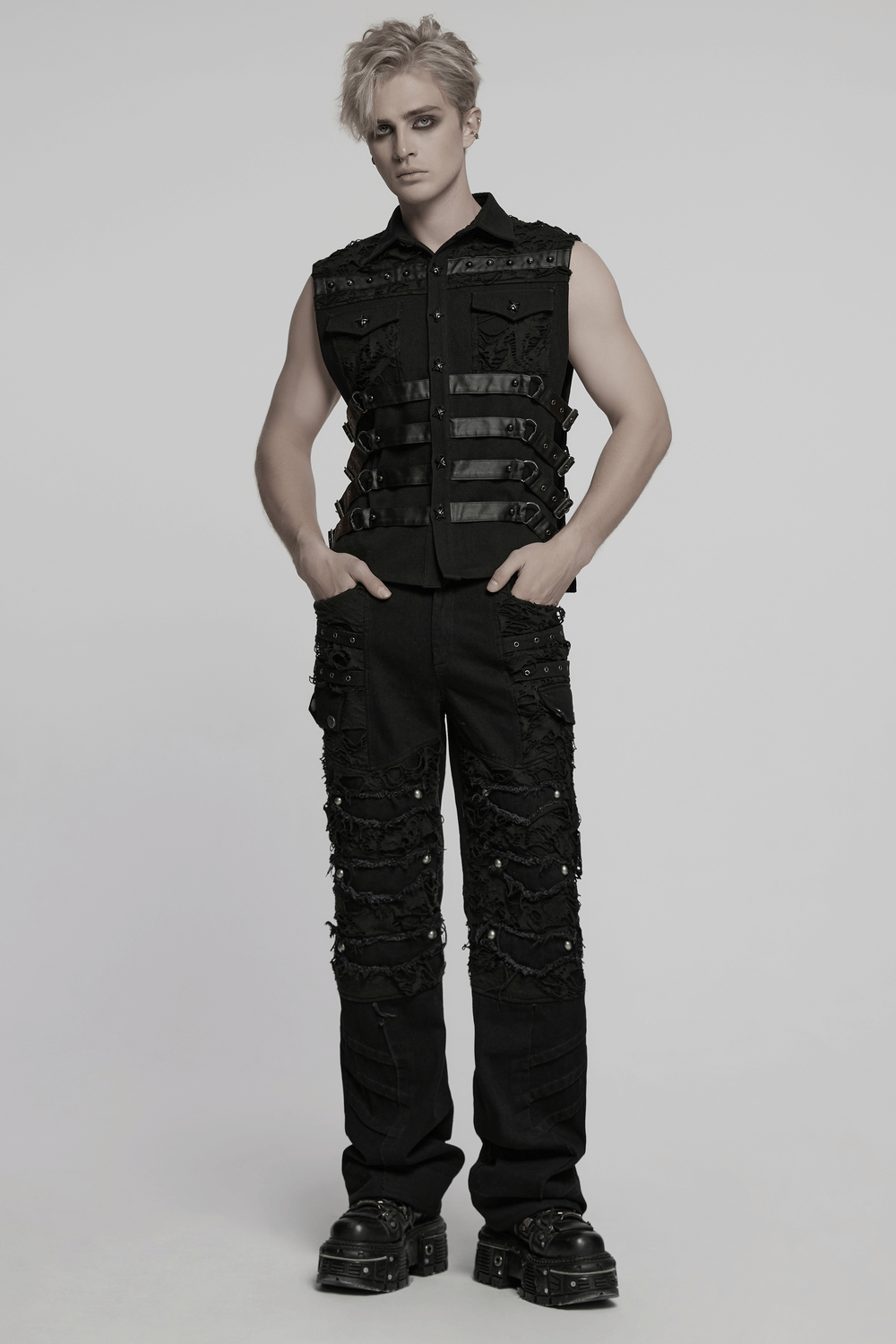 Edgy model wearing black punk pants with tassels, distressed mesh, and a vest featuring straps, showcasing a rebellious look.