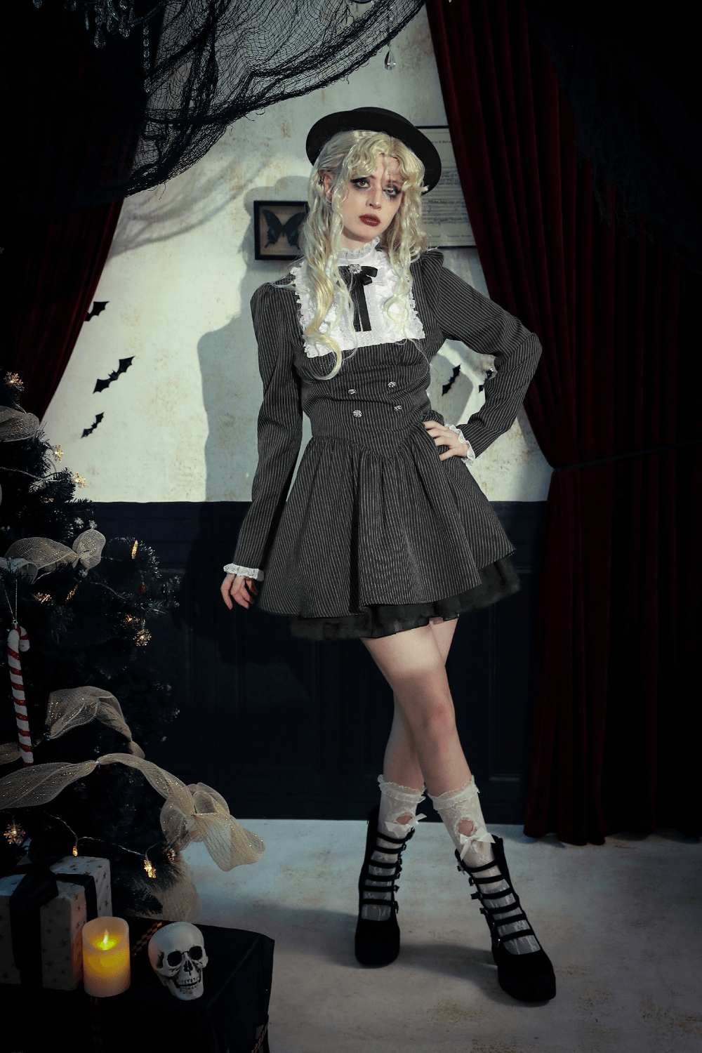 Stylish model in pinstripe gothic dress with lace ruffle and bow, posing in a vintage-inspired room with festive decor.