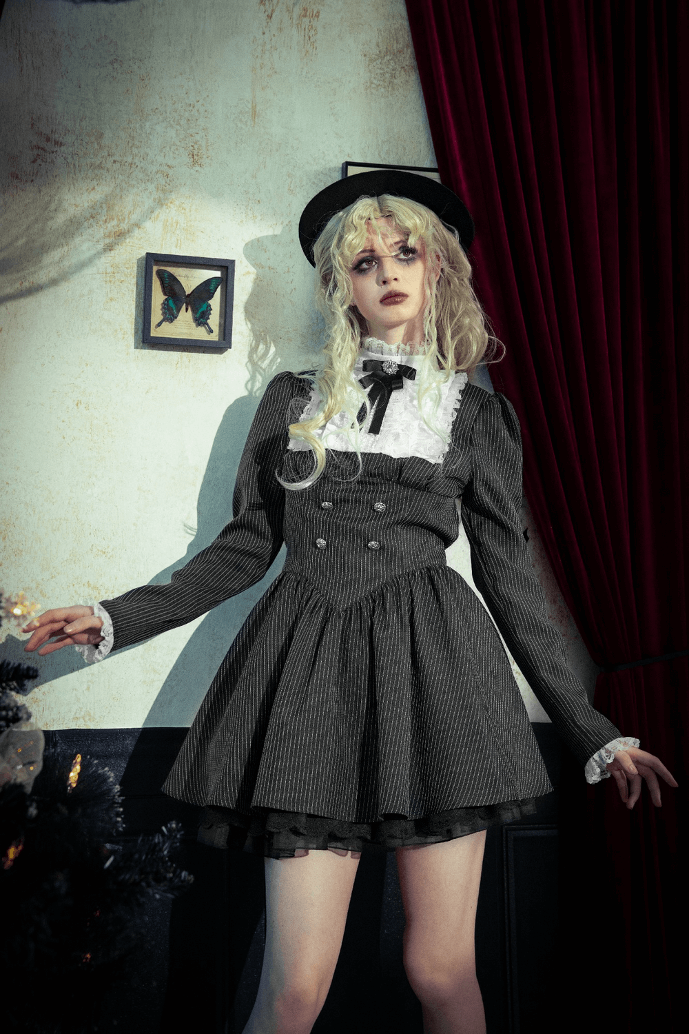 Stylish model in a pinstripe gothic dress with lace ruffle and bow, posing elegantly in a vintage-inspired setting.