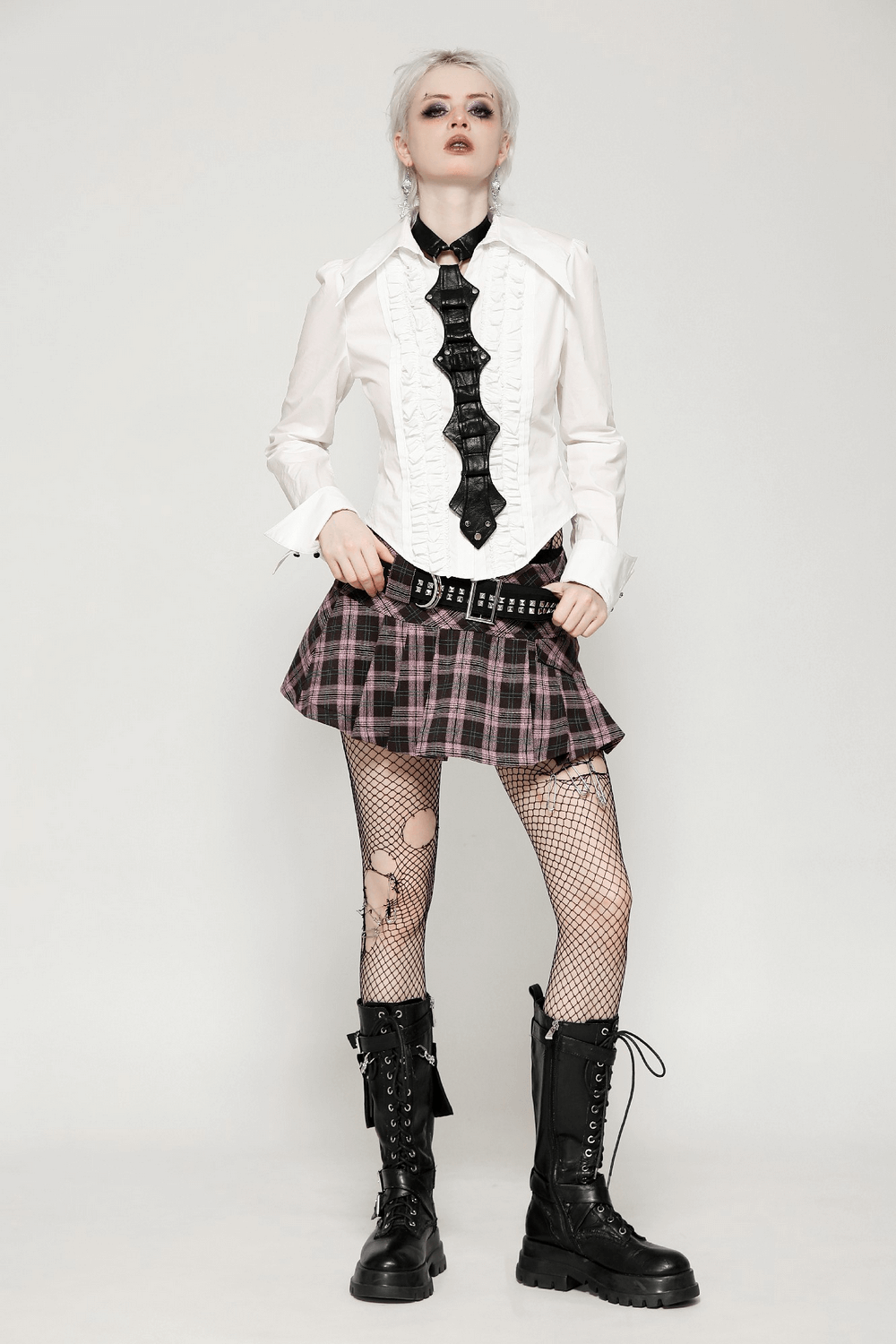 Trendy model wearing a plaid mini skirt with studded belt, edgy black fishnet stockings, and combat boots, showcasing a bold style.
