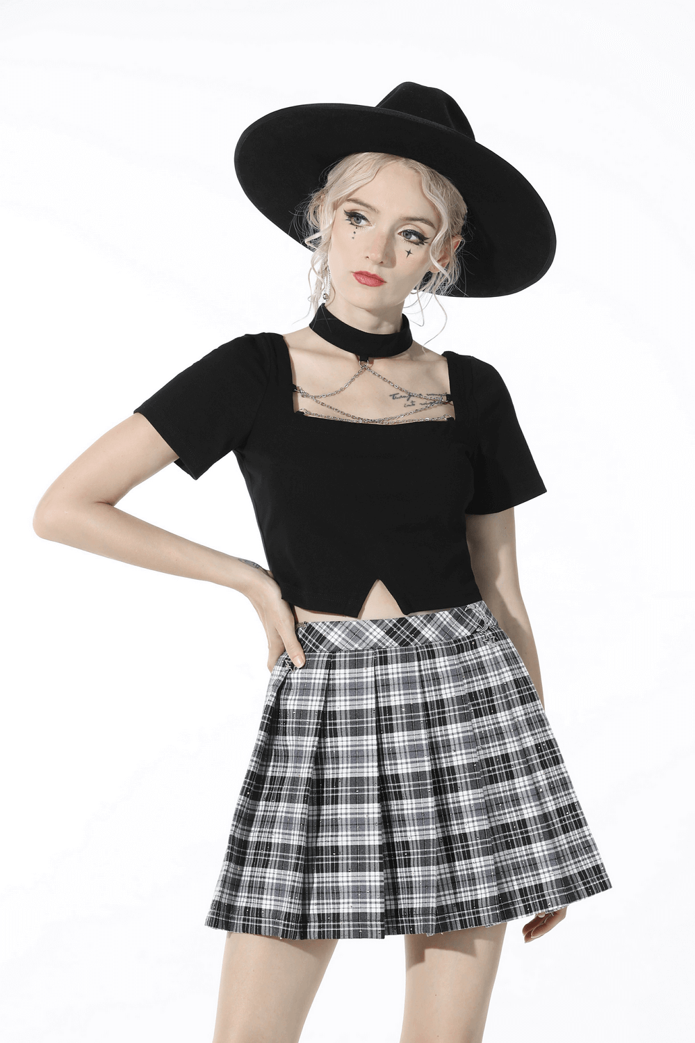 Model wearing a black and white plaid pleated mini skirt with a stylish black top and chic wide-brim hat.