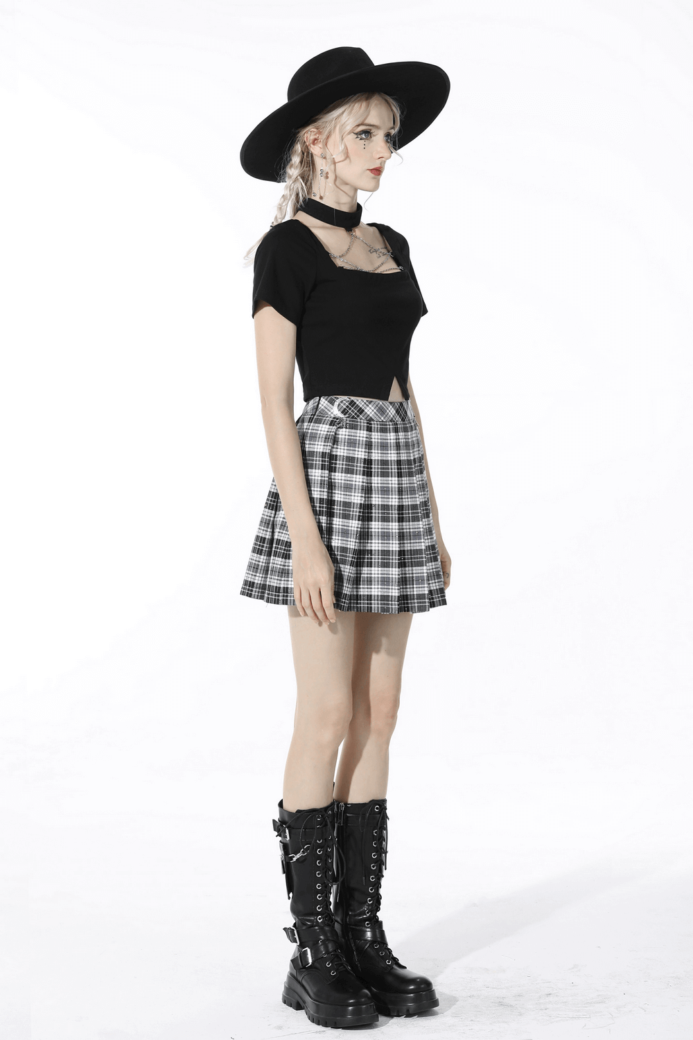 Edgy fashion model in black and white plaid pleated mini skirt, black top, hat, and combat boots for a punk look.