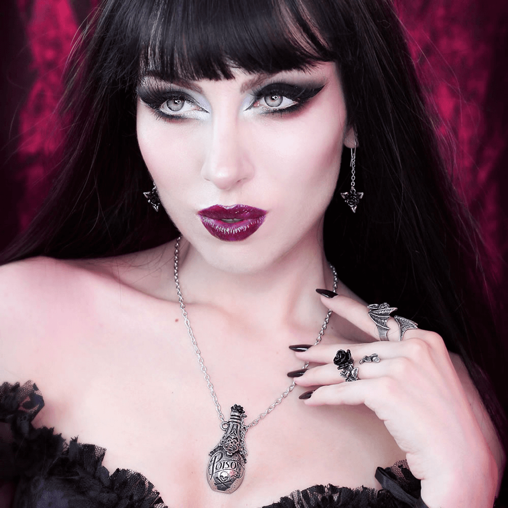 Model showcasing vintage poison bottle pendant necklace with skull and black rose against a dramatic backdrop.