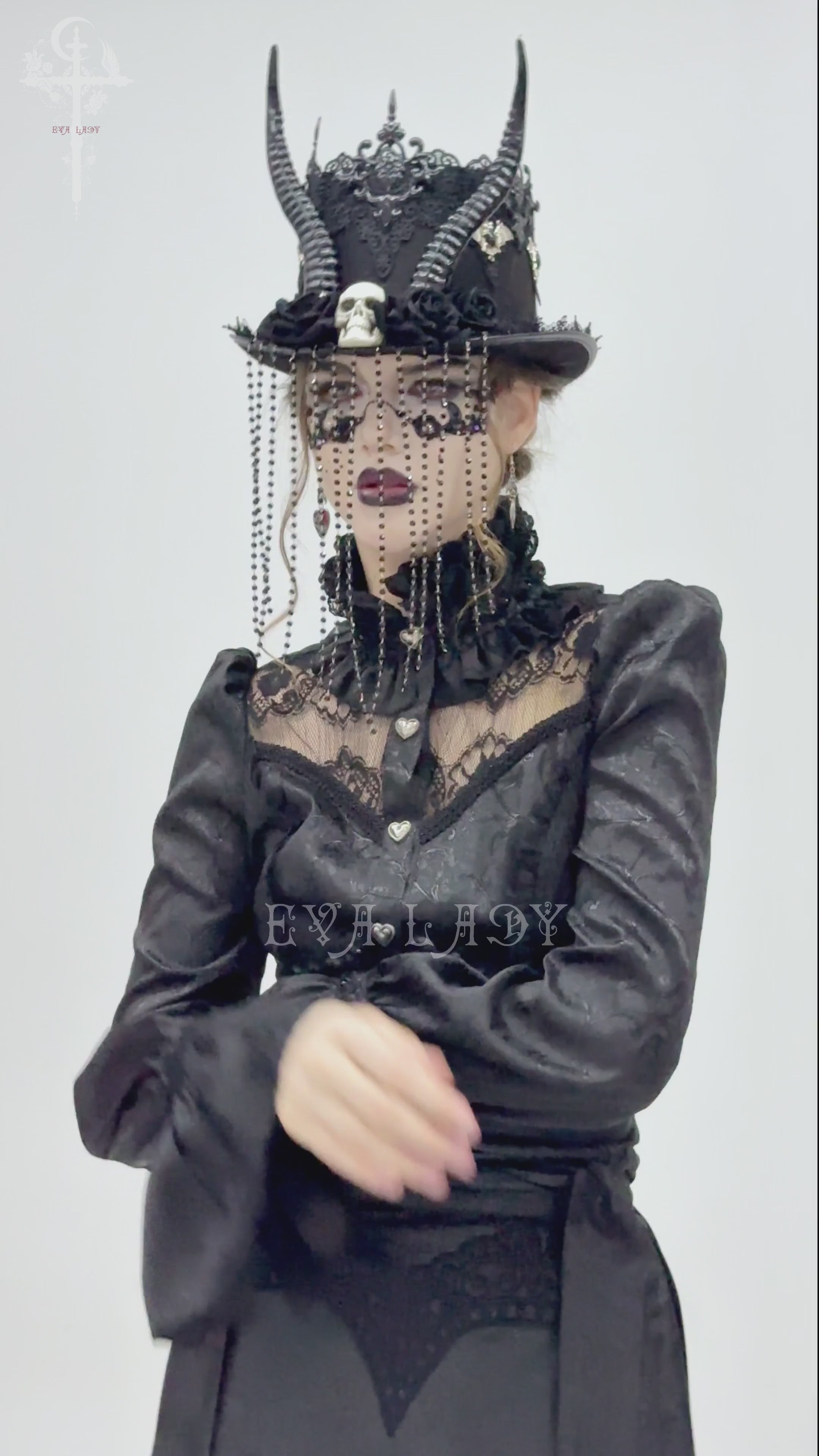 Gothic black horned top hat adorned with skull, beads, and lace worn by a model in elegant dark attire.