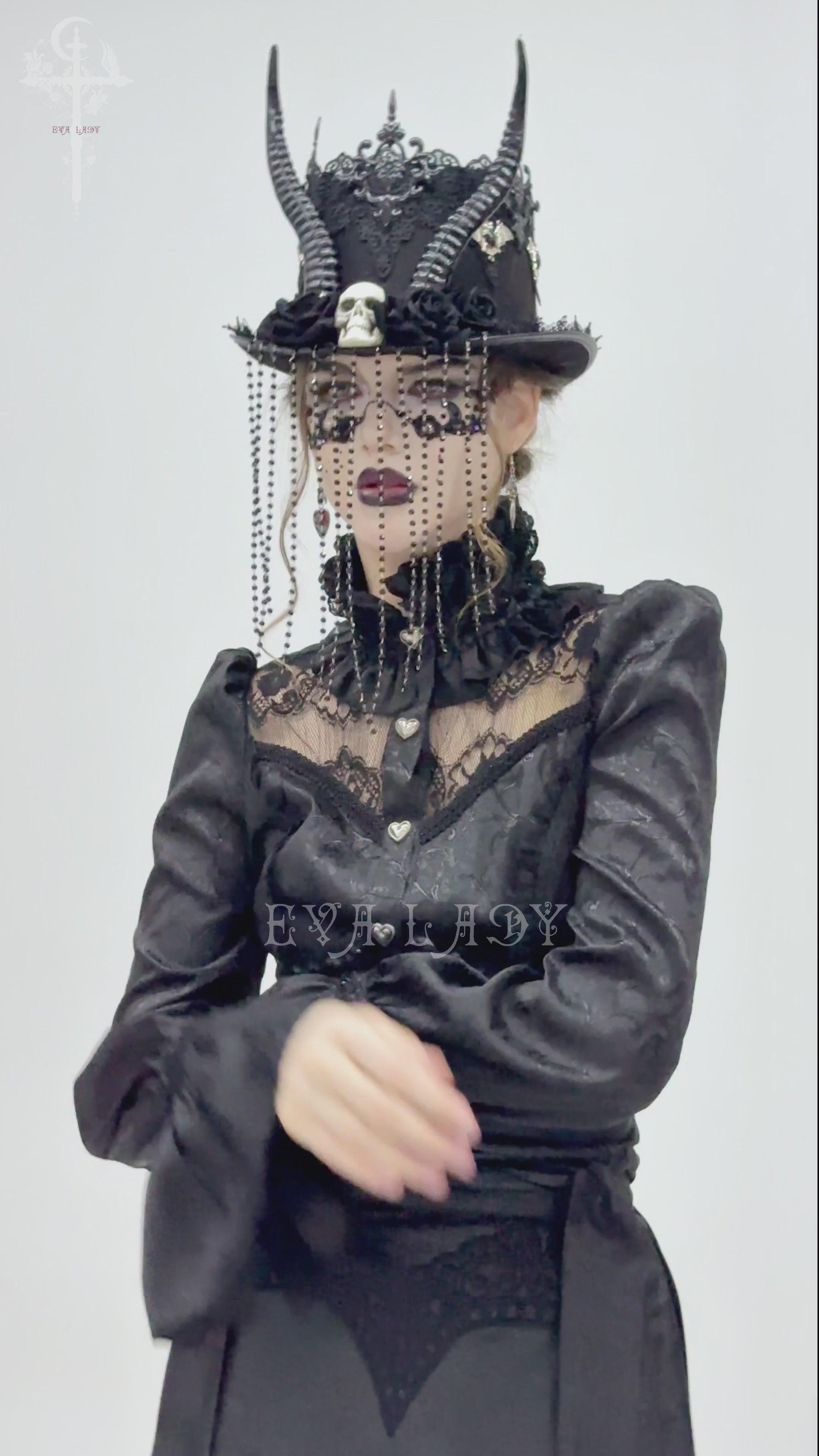 Gothic black horned top hat adorned with skull, beads, and lace worn by a model in elegant dark attire.