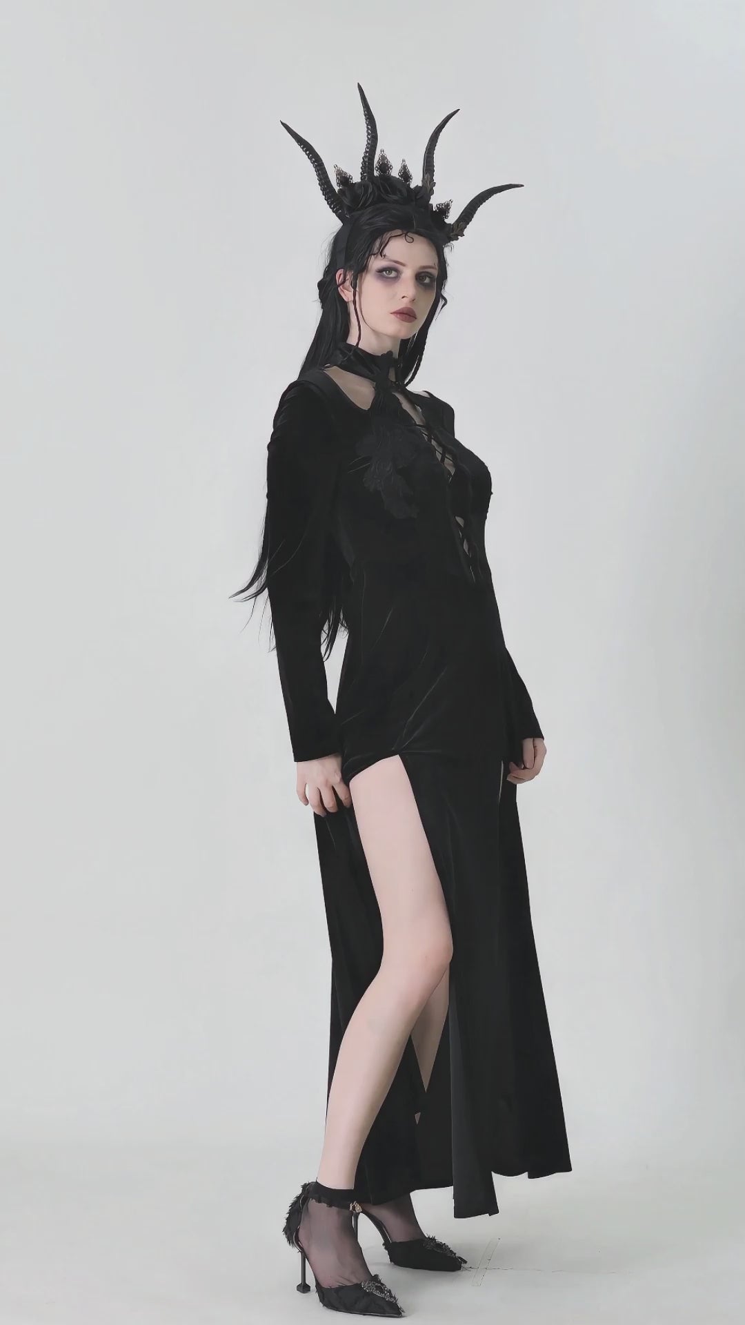 Model wearing a gothic lace-up velvet dress with ruffled details and a high slit, styled with dramatic horns.