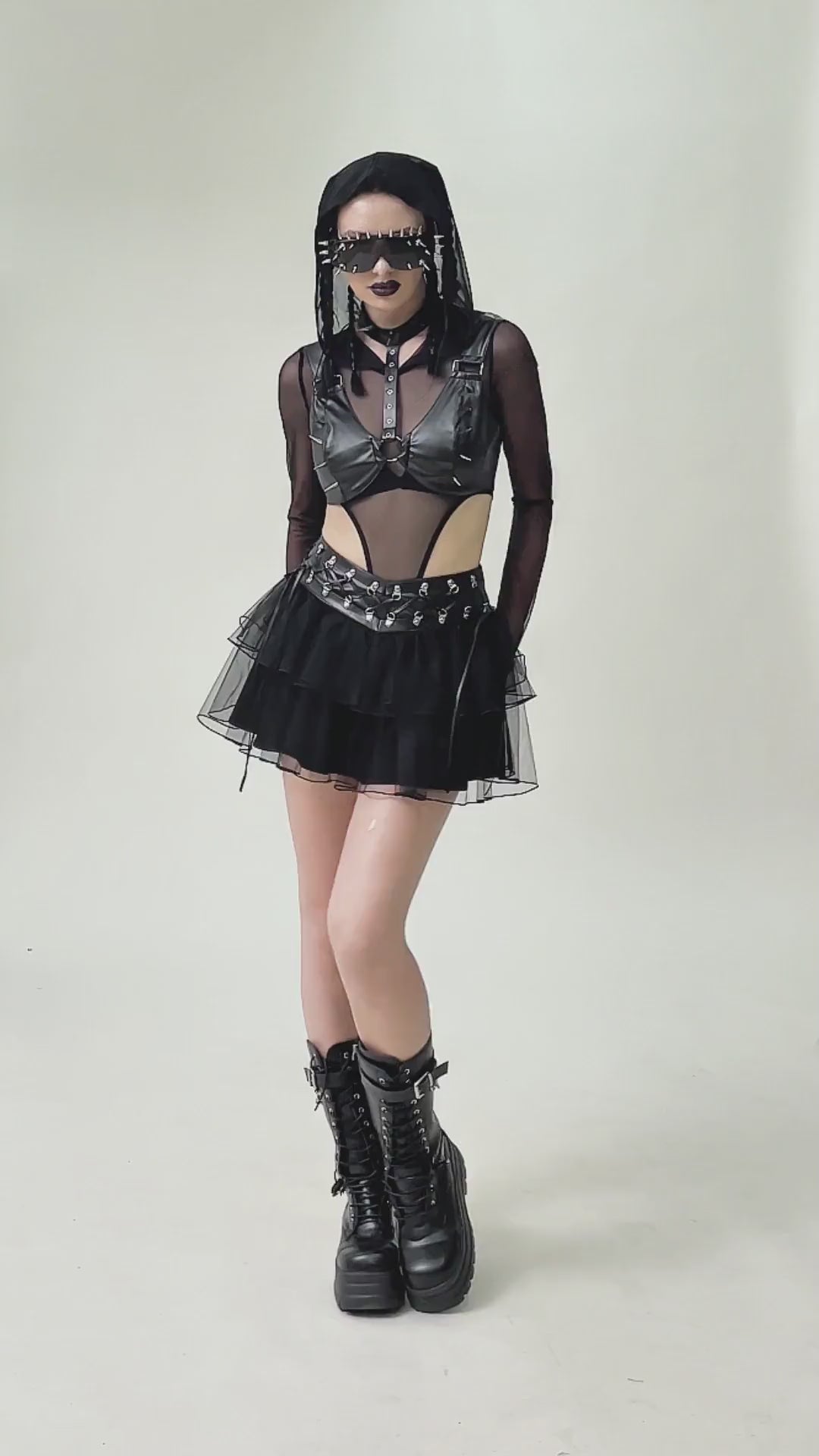 Model wearing a bold gothic punk outfit with a faux leather harness bra, layered tulle skirt, and edgy knee-high boots.