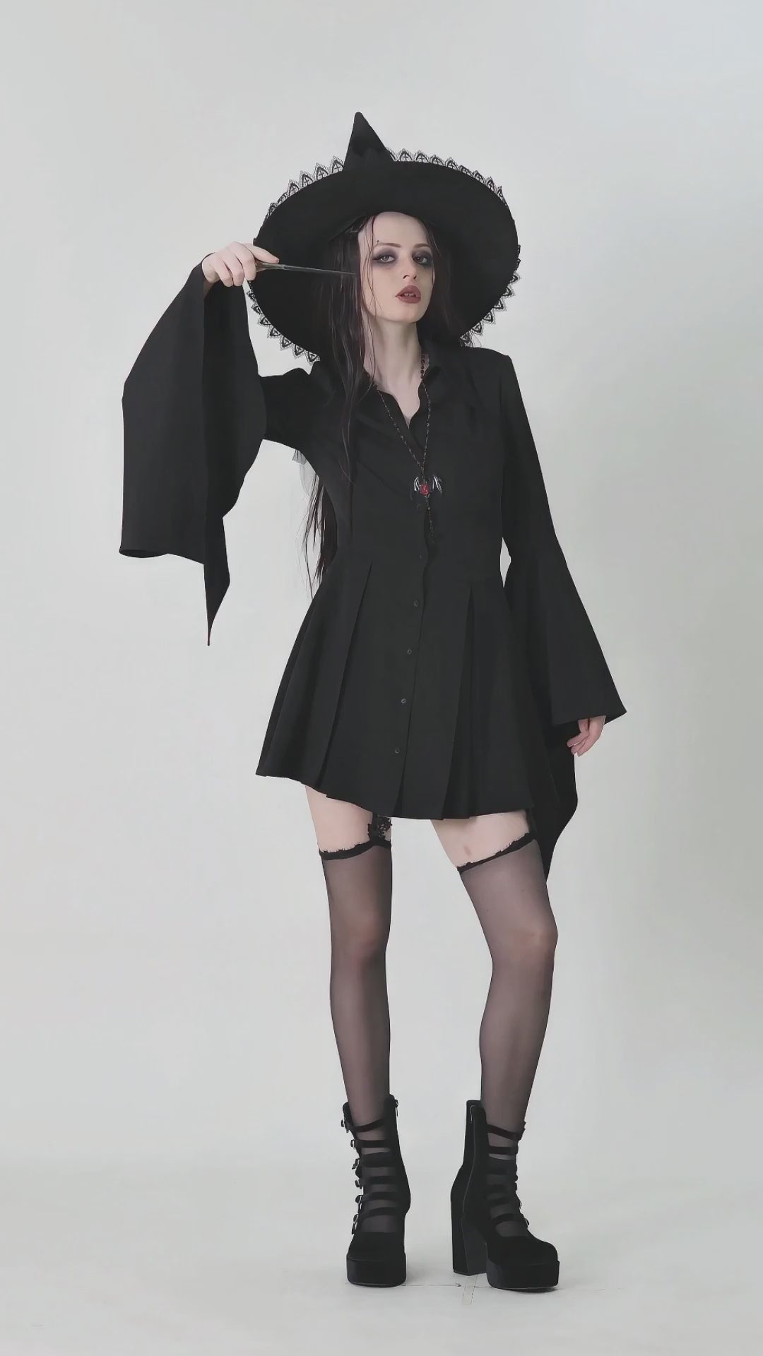 Model in a dark gothic dress with flared sleeves and a witch hat, capturing alternative fashion vibes.