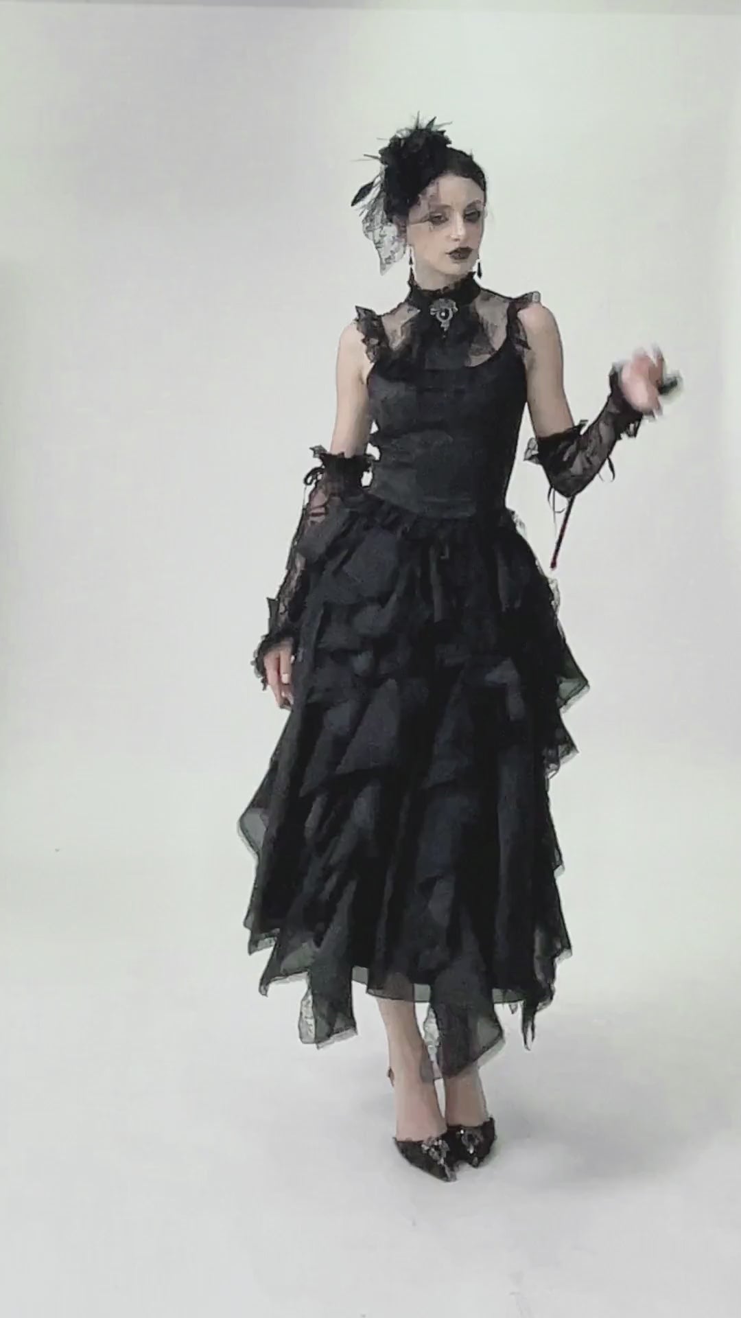 Elegant gothic woman in a black lace blouse with ruffled skirt, adorned with a feathered headpiece and dramatic makeup.