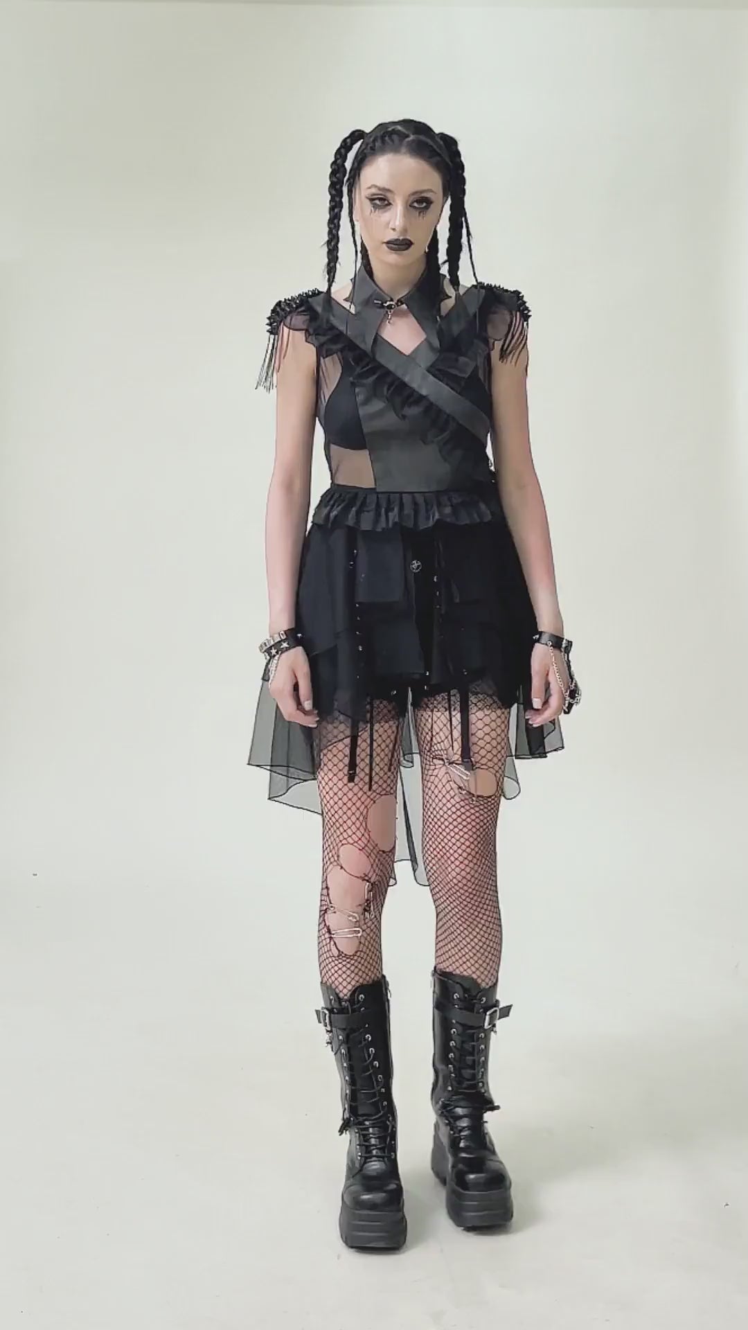 Edgy female model in a gothic black lace-up tulle dress with ruffles, fishnet tights, and combat boots, showcasing a dramatic style.