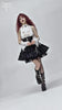 Gothic fashion model in a black skirt and white lace top with dramatic makeup and bold black boots.