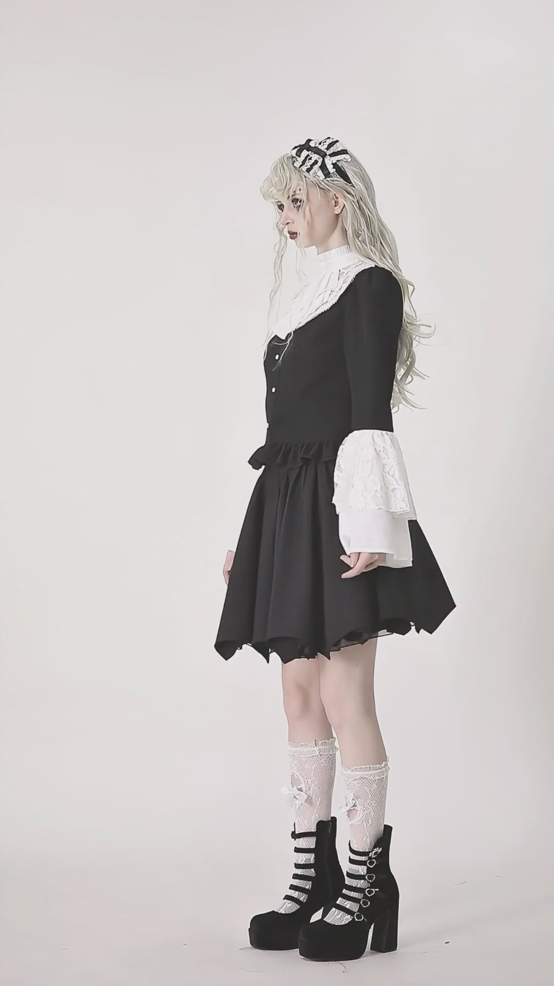 Side view of a woman in a vintage black dress with white lace sleeves, styled with stylish boots and a headband.
