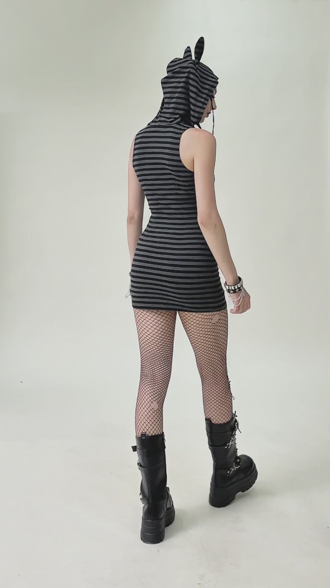Back view of a striped Gothic hooded dress with devil ears, paired with fishnet tights and combat boots.