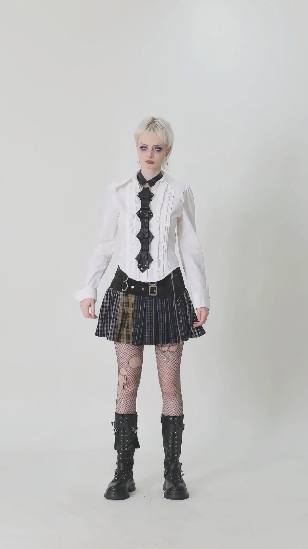 Model wearing a stylish punk outfit with a white blouse, black skirt, fishnet tights, and combat boots, showcasing edgy fashion.