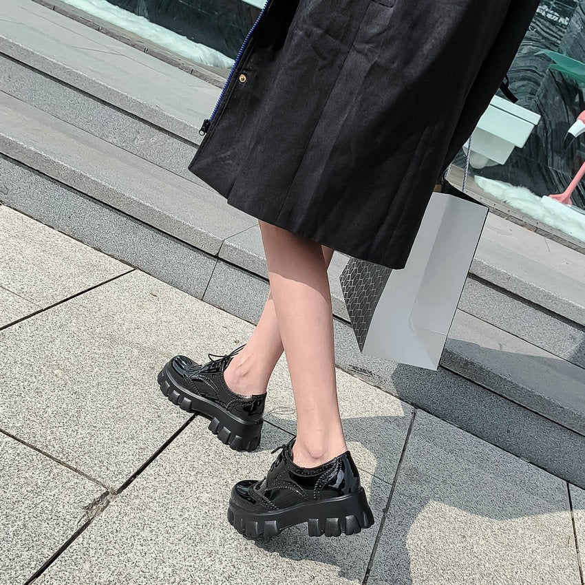 Black PU leather platform women's shoes with square heel, styled with a long black coat on a city sidewalk.
