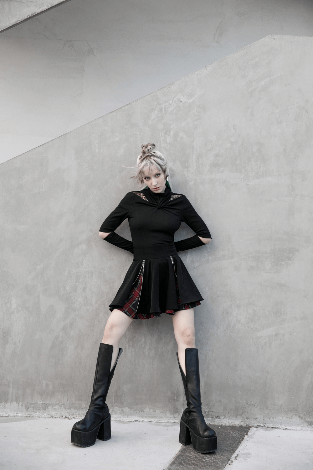 Model wearing a punk A-line skirt with plaid detail and stylish tall boots, posing against a modern concrete background.