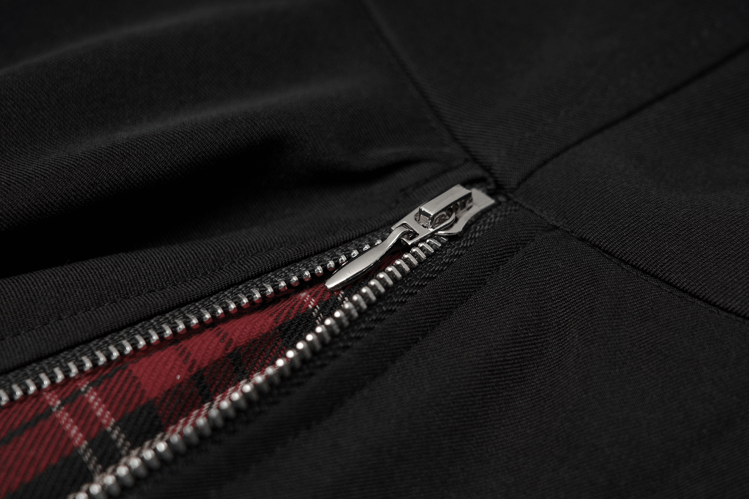 Close-up of a stylish zipper on a black skirt, showcasing bold red and black plaid detail for a punk aesthetic.
