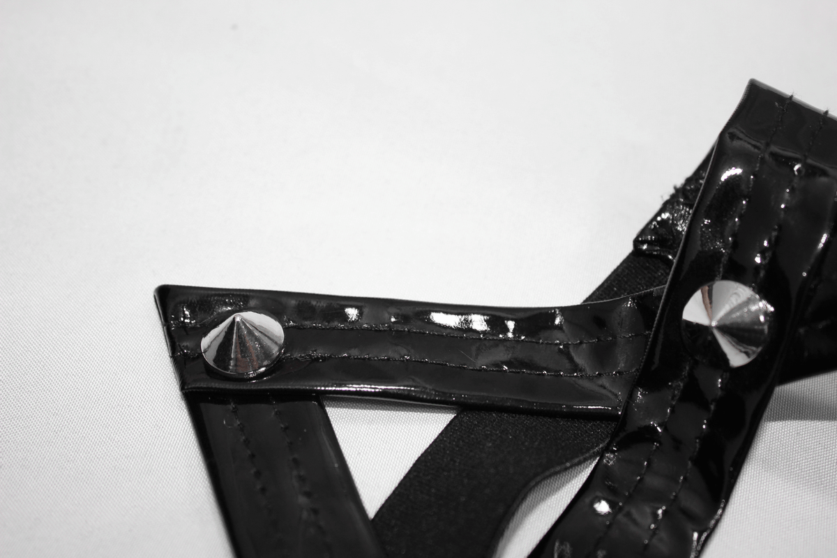 Close-up of shiny black pentagram harness belt detail with silver rivets, perfect for punk-style outfits.
