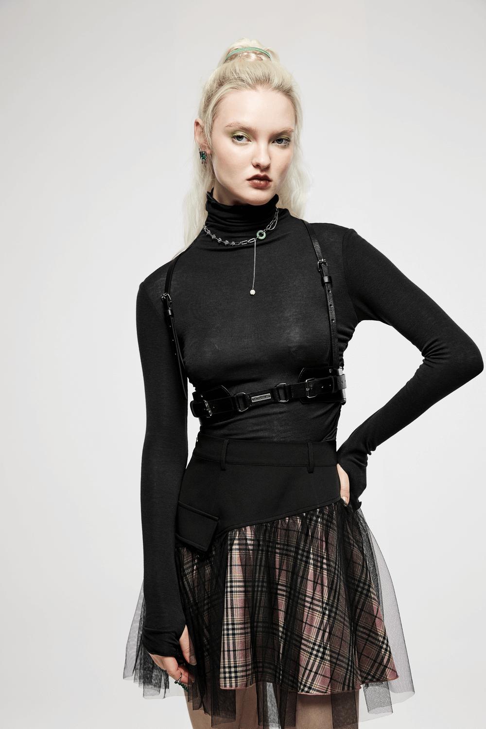 Model wearing a Punk Bold PU leather harness with metal detailing over a black top and plaid skirt.