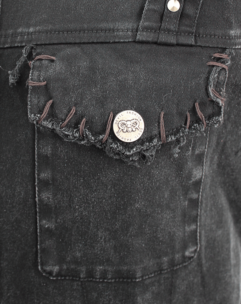 Close-up of black denim vest pocket with frayed edges and silver button, showcasing punk style design.