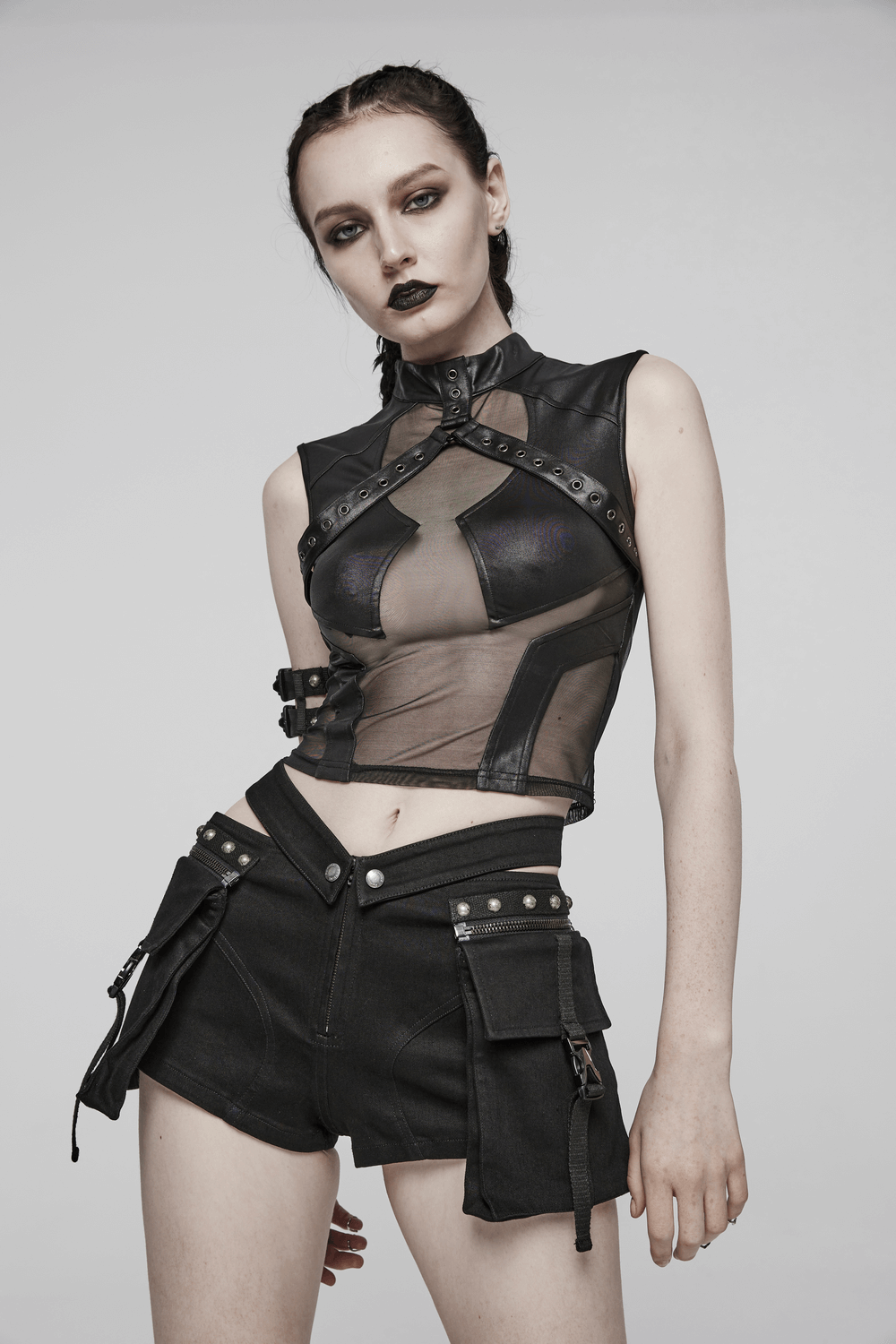 Stylish model in sheer punk top and black riveted shorts with detachable cargo pockets, showcasing edgy fashion.