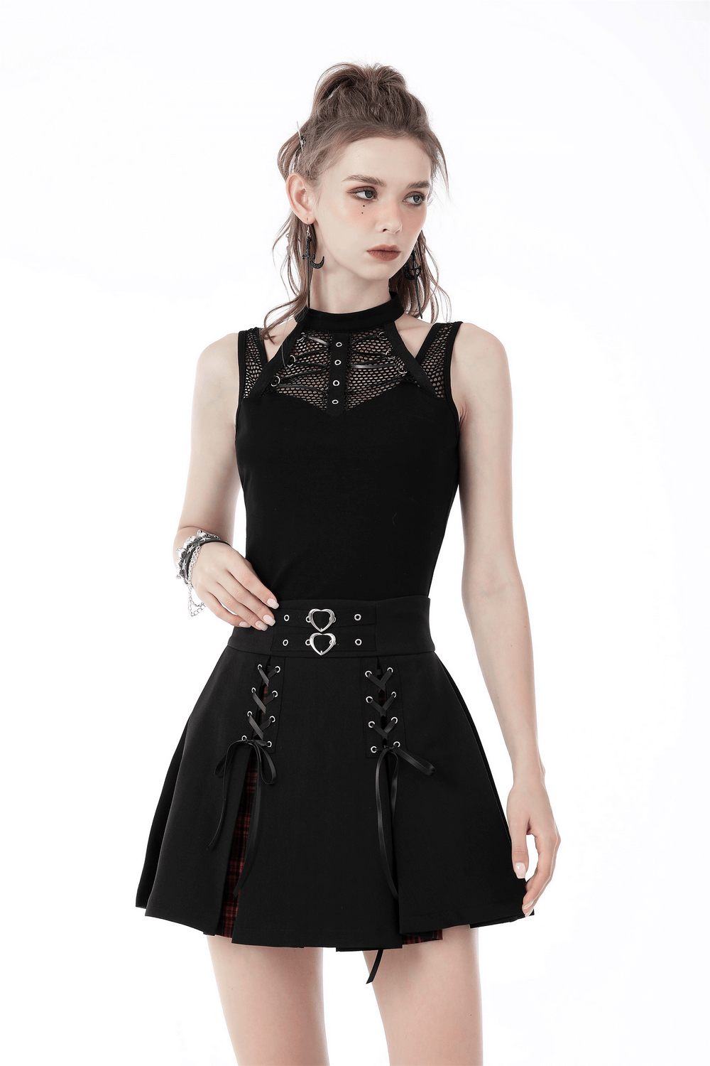 Edgy punk female model wearing a black sleeveless crop top with ribcage mesh and a stylish skirt with lace-up accents.