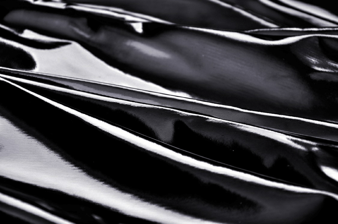 Close-up of glossy black patent leather fabric, showcasing its sleek texture and shine.