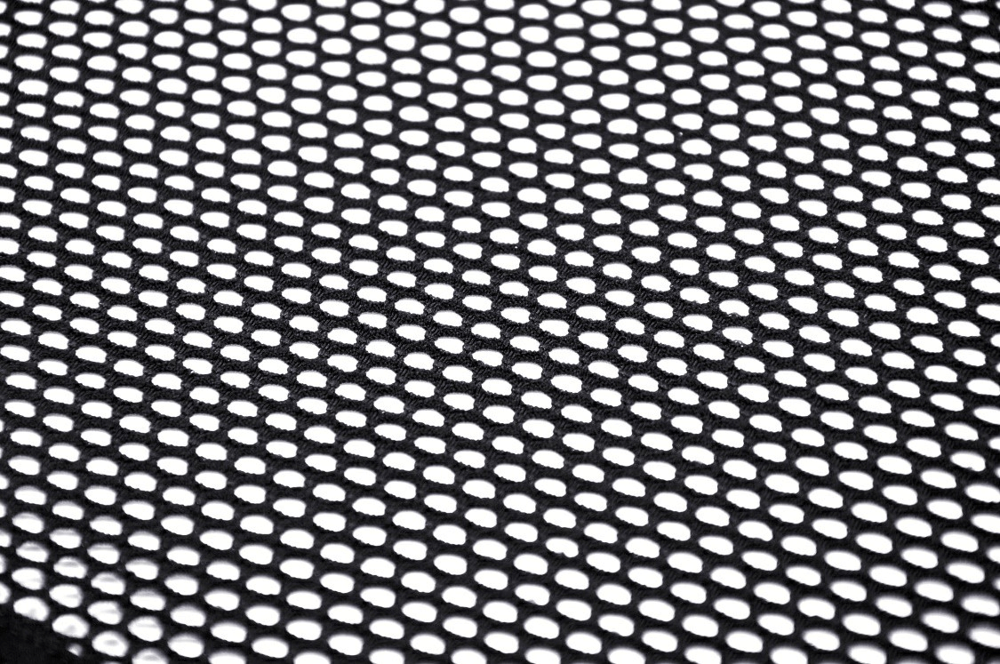 Close-up of black sheer mesh fabric with circular holes, perfect for punk gothic fashion and edgy style.