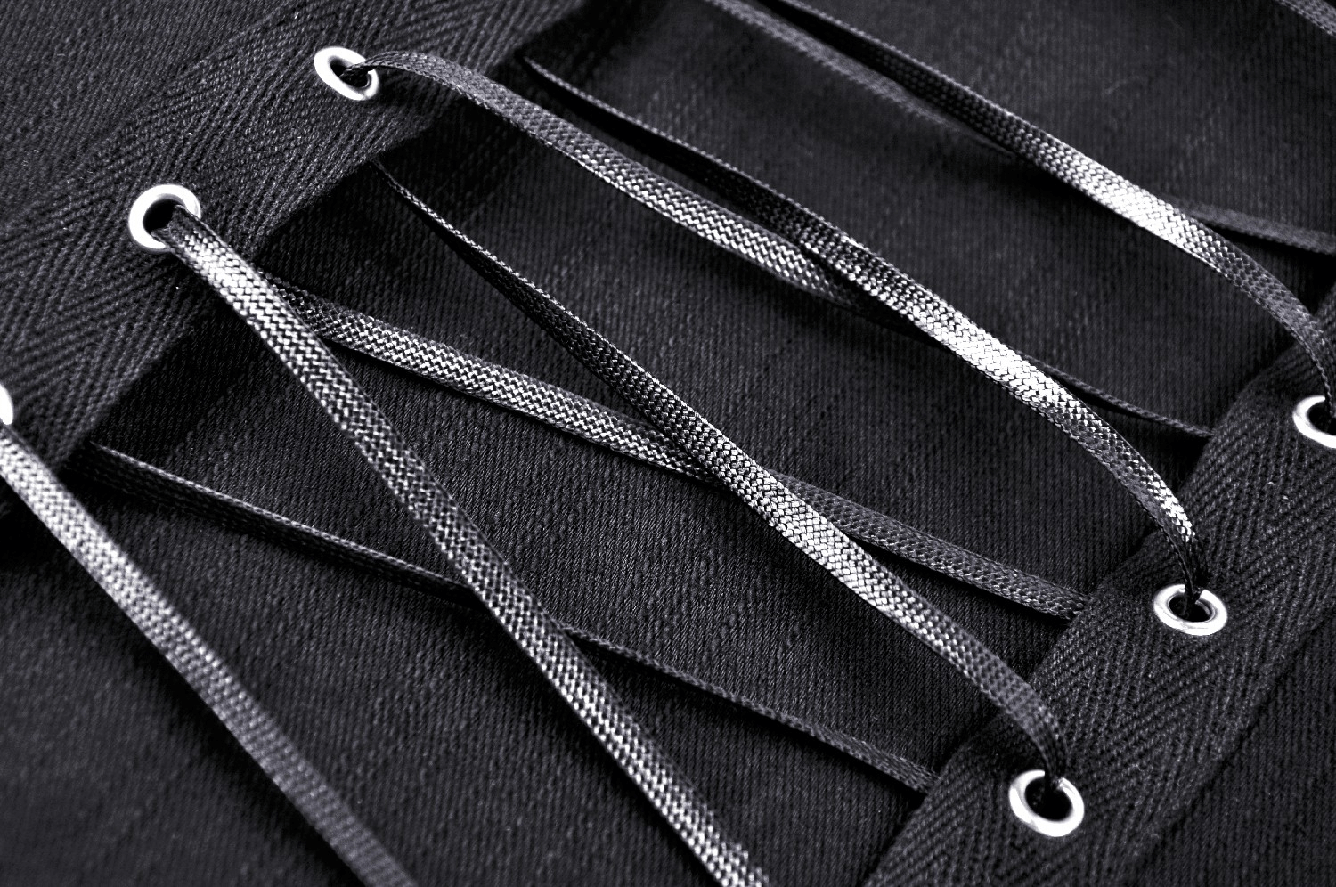 Close-up of black lace-up corset detailing with metallic eyelets and straps for a punk rock style.