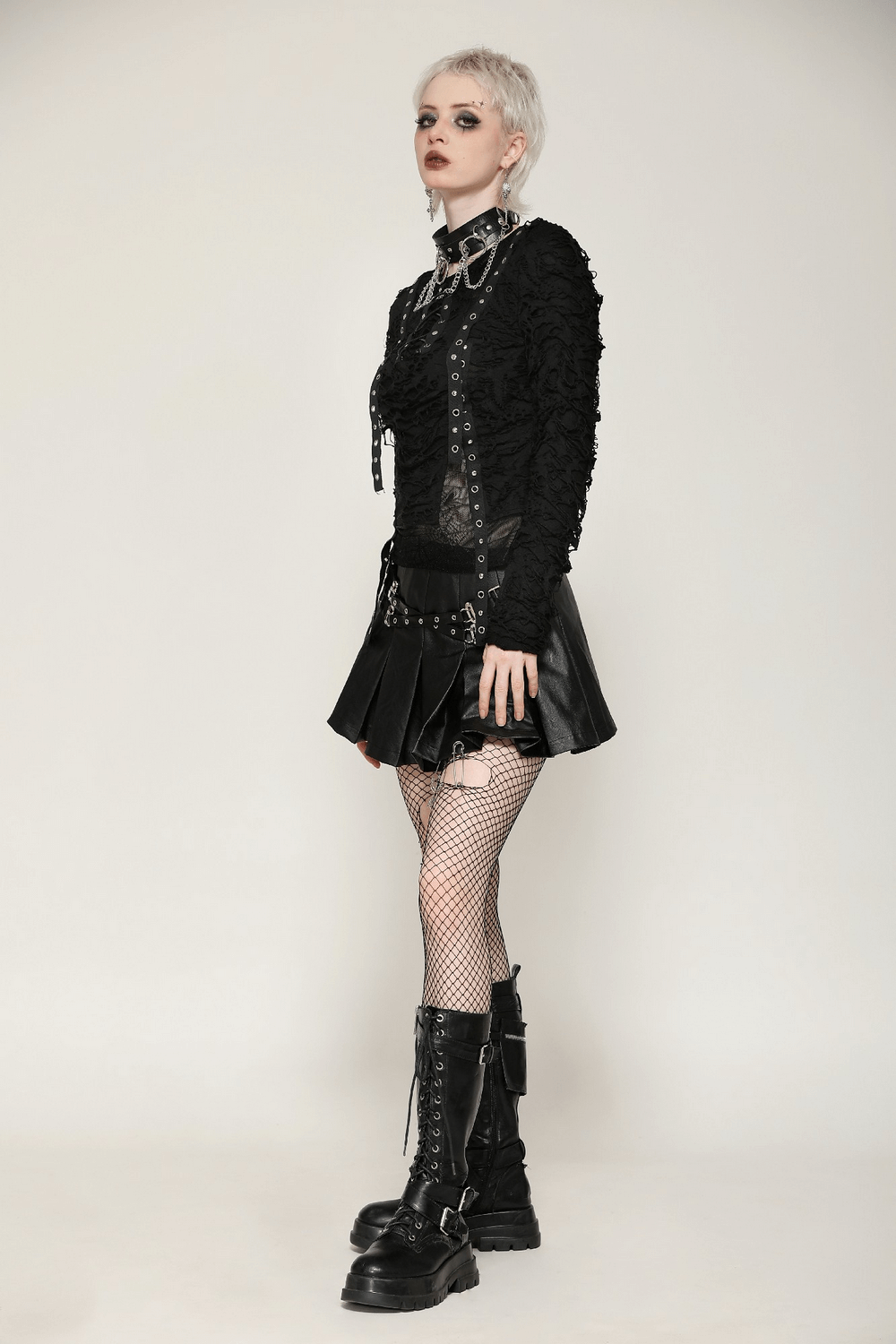 Edgy punk model in lace-up black mesh top and leather skirt with fishnet tights and combat boots, showcasing alternative fashion.