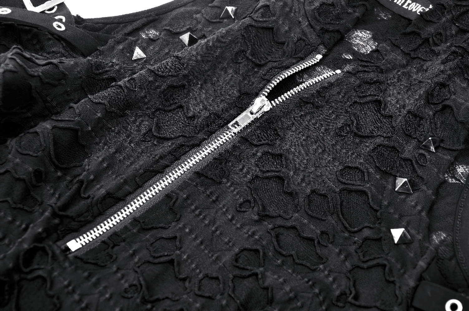 Close-up of black lace fabric with zipper and studs, highlighting punk style and edgy fashion.