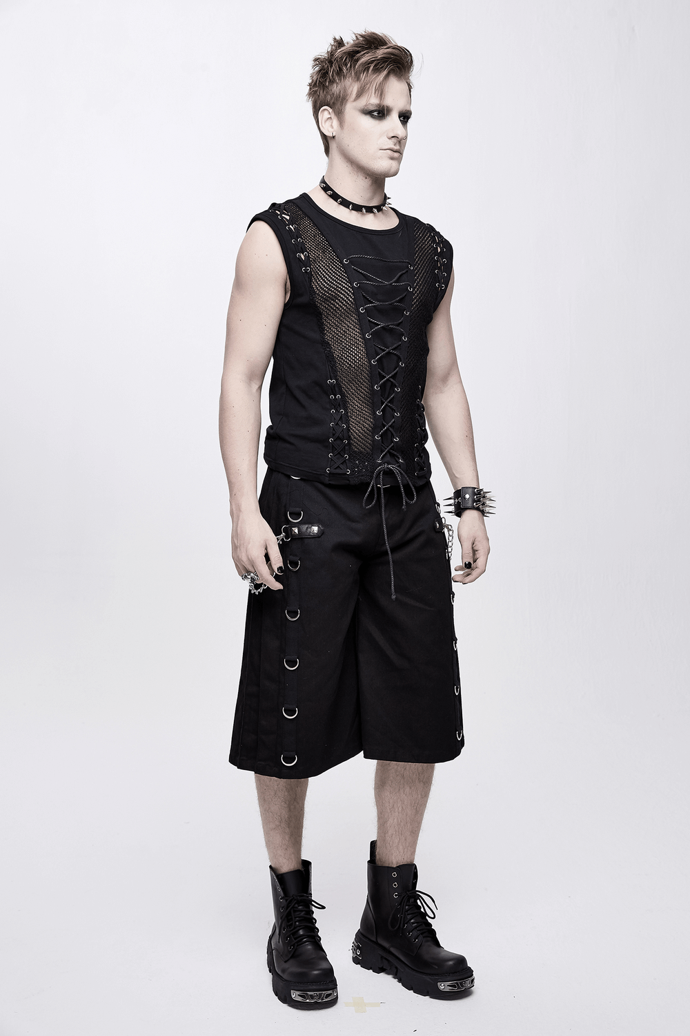Stylish punk man wearing a black sleeveless tank top with mesh and drawstring, paired with black shorts and boots.