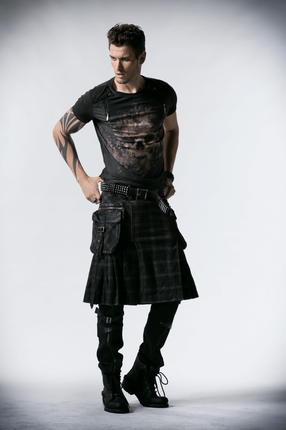 Stylish man wearing a punk plaid kilt with cargo pockets, black t-shirt, and edgy boots, showcasing a modern alternative look.