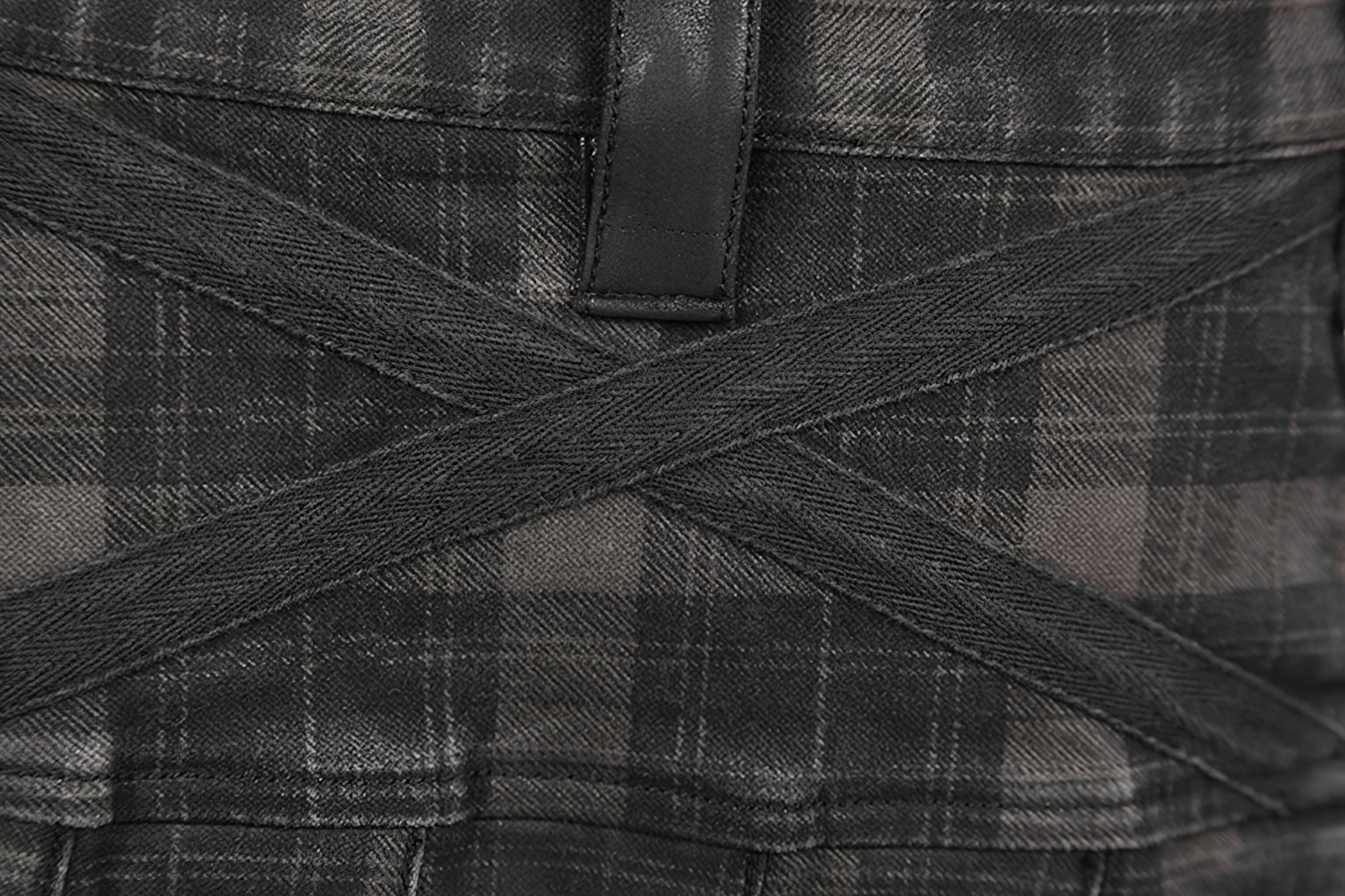 Close-up of black plaid kilt with stylish crisscross design and straps for a bold punk look.