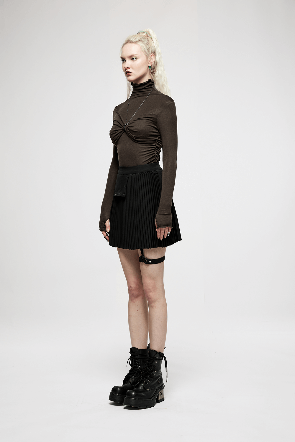 Model showcasing a dark punk pleated asymmetric skirt with engraved nails and a fitted brown top. Perfect for edgy style.