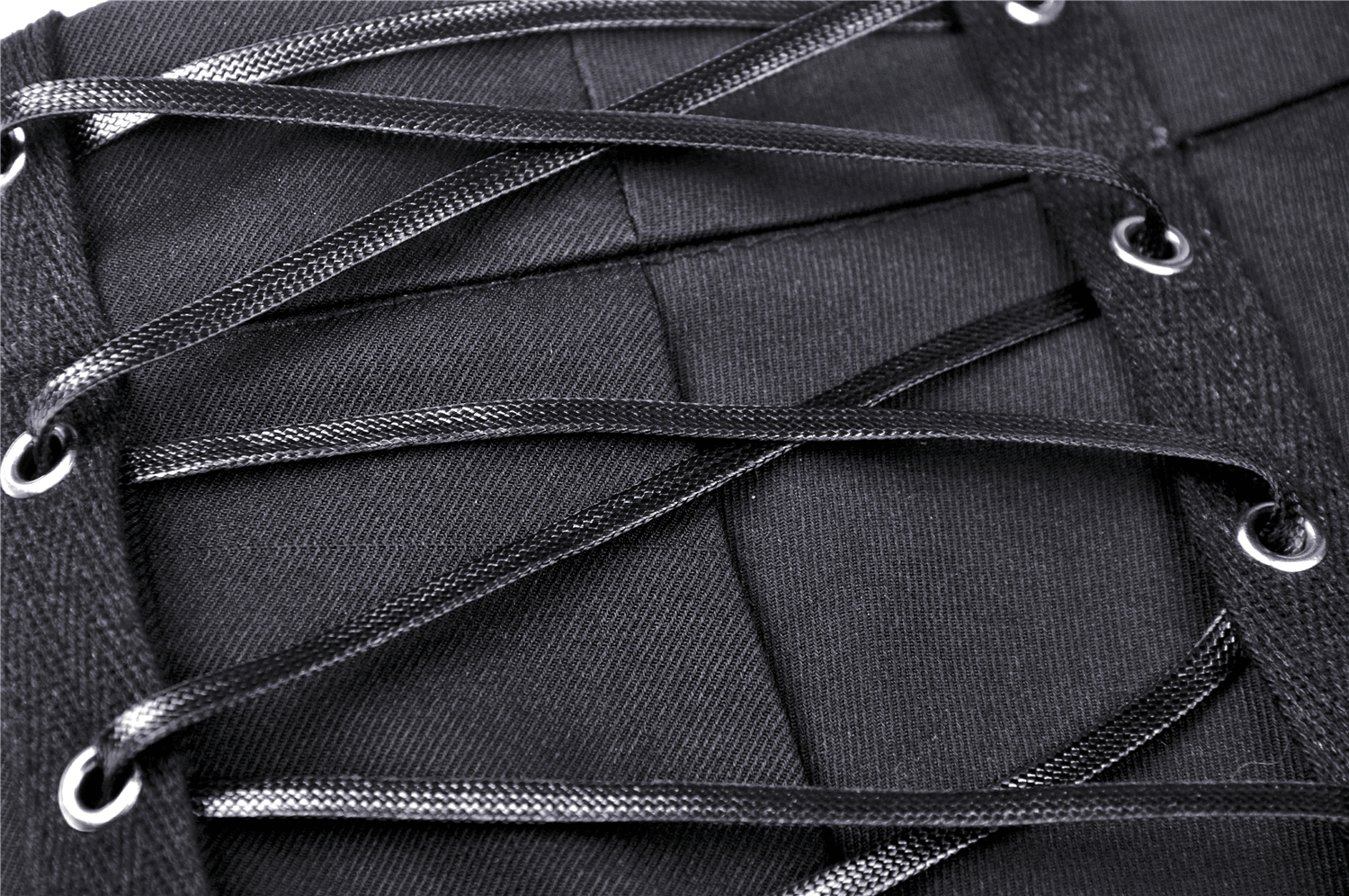 Detailed view of black laces and grommets on a punk mini skirt, showcasing edgy design elements.