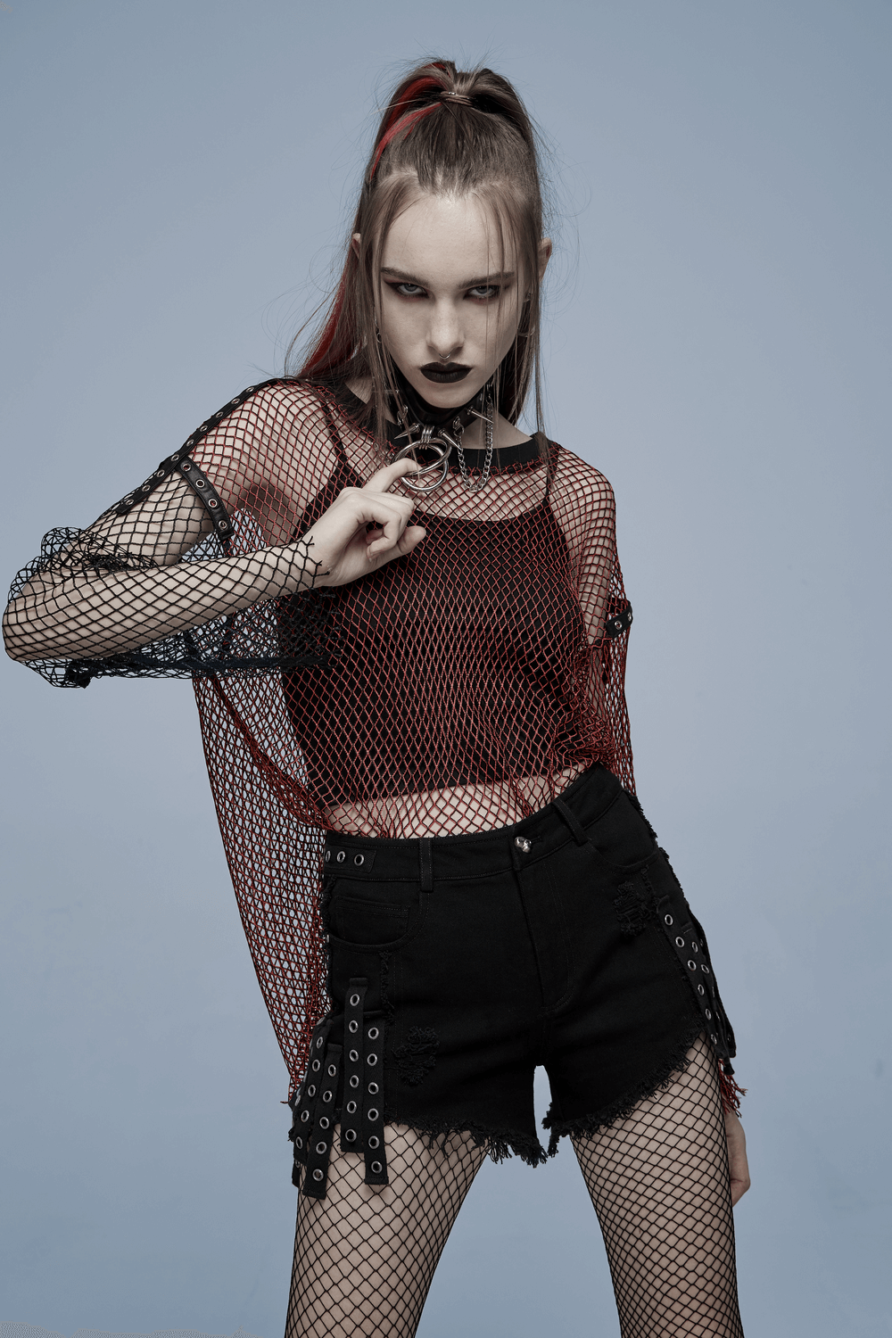 Model wearing punk rave black denim shorts with edgy detailing and a red fishnet top for a rebellious look.