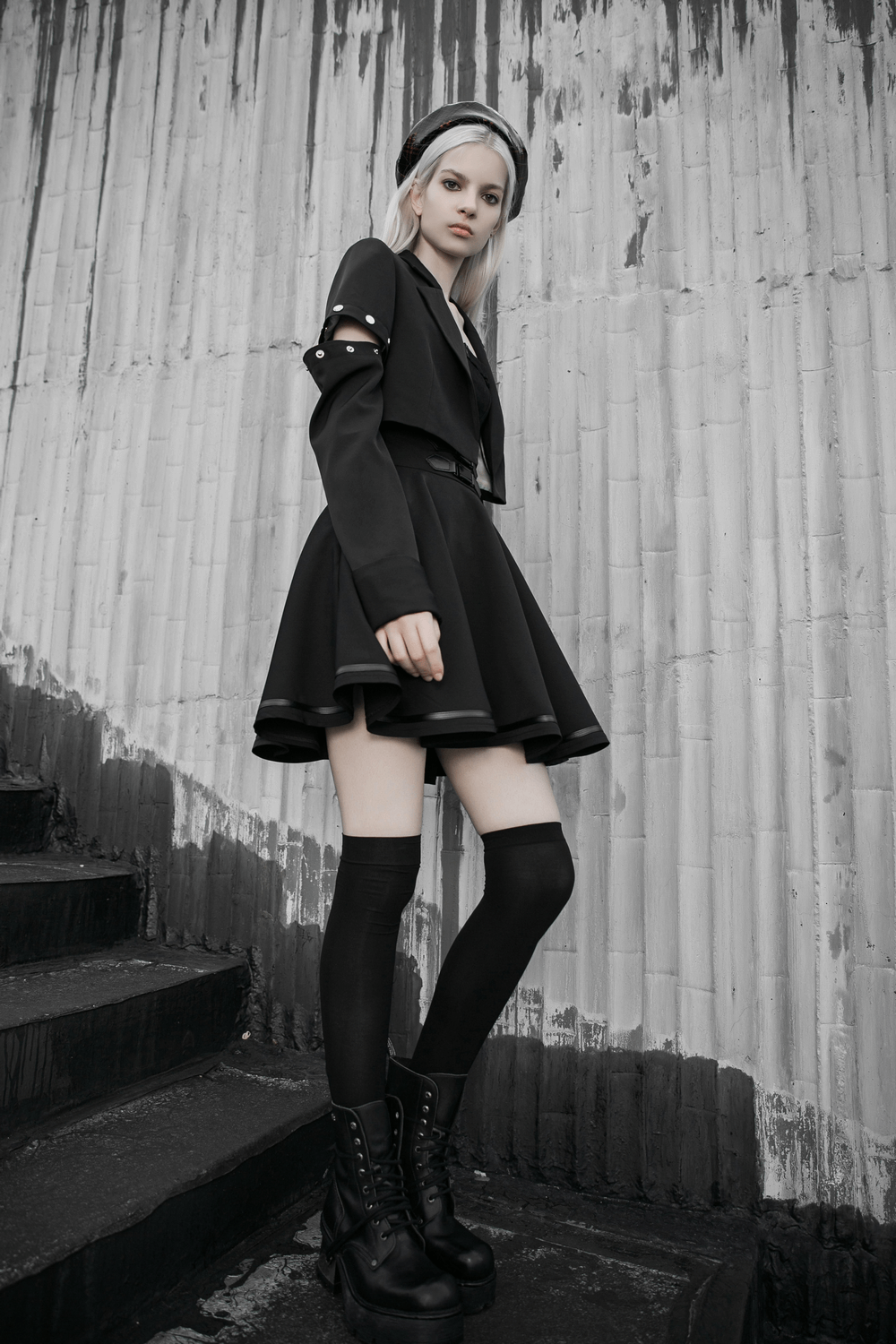 Edgy model in a black high-waisted skirt with buckle, styled with knee-high socks and chunky boots.