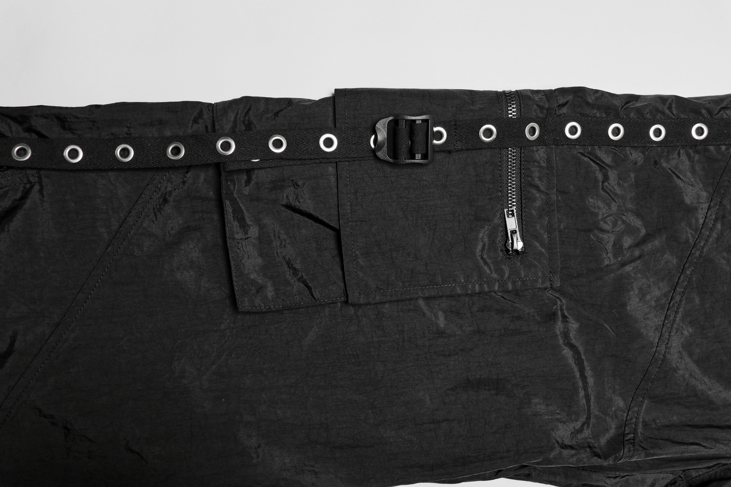 Black tactical cargo pants close-up showcasing eyelet webbing, metal buckle, and decorative zipper.
