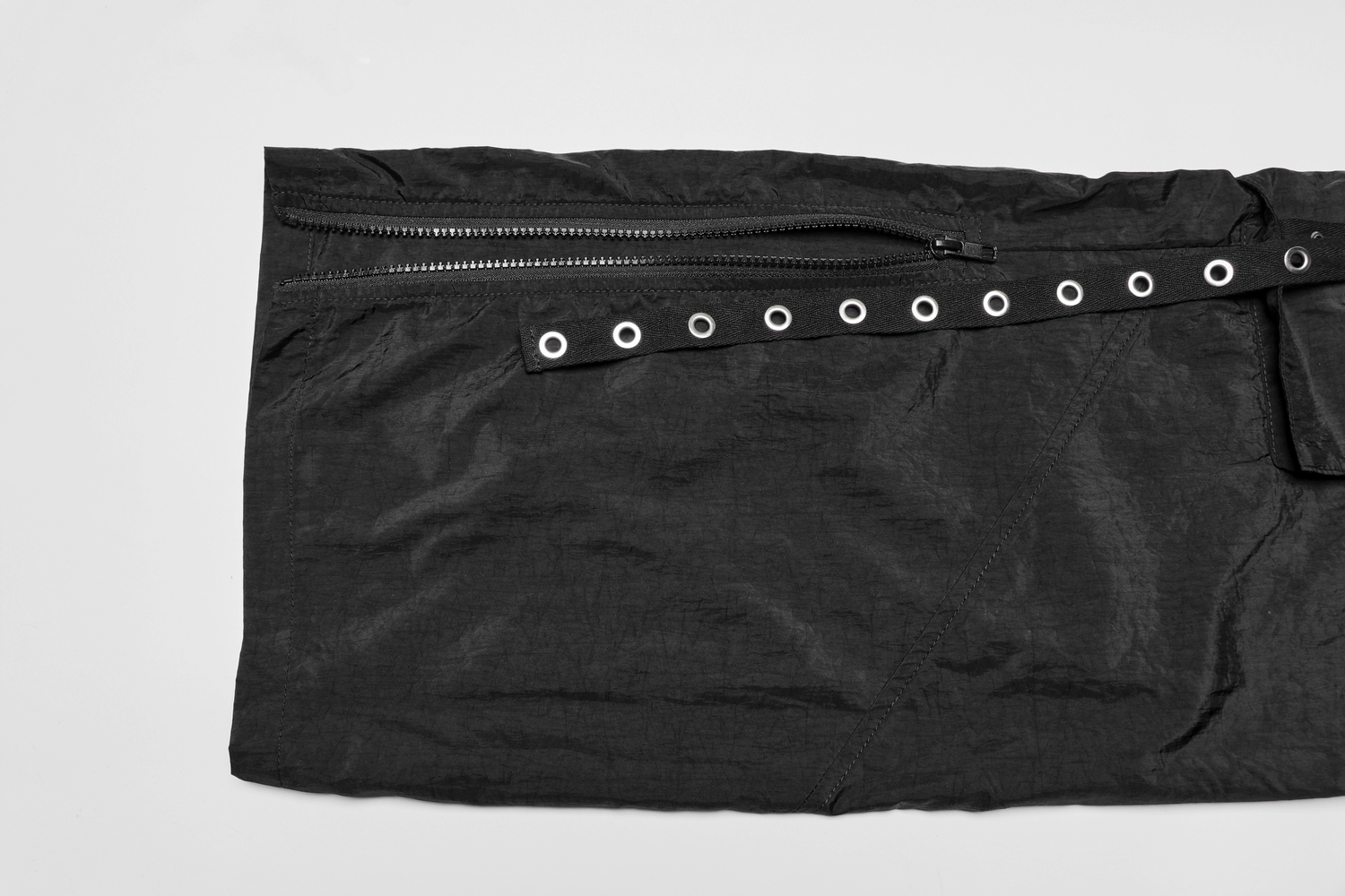 Close-up of black cargo pants fabric featuring eyelet webbing and decorative zipper.