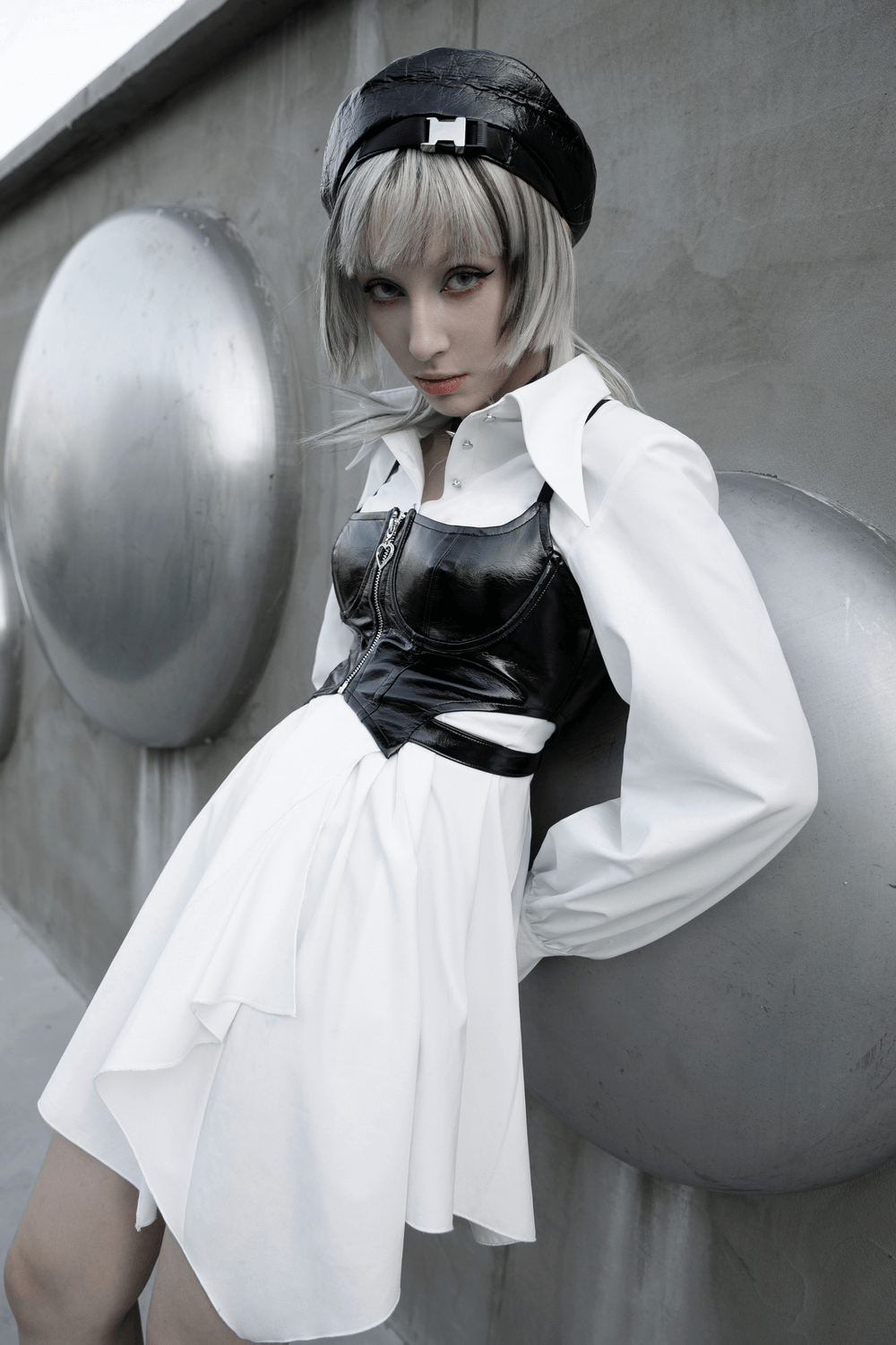 Model in a punk rave gothic white swallowtail shirt dress with asymmetrical hem, styled with a black corset and hat.
