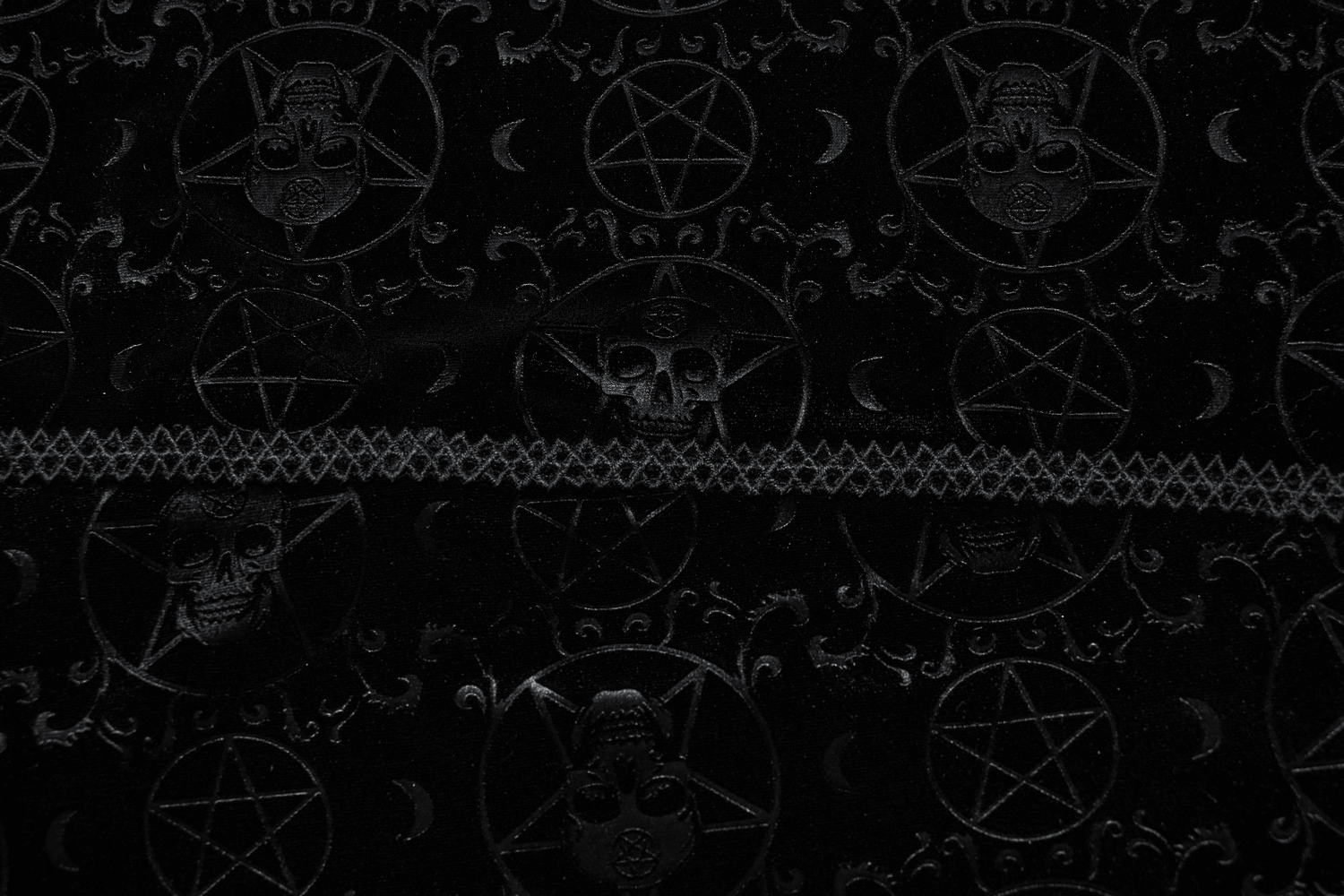 Close-up of black embossed velvet fabric featuring pentagrams and skulls, perfect for a gothic cape.