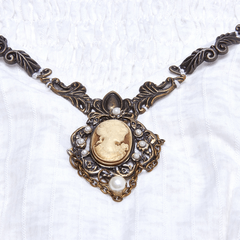 Vintage metal necklace with a cameo, pearls, and intricate detailing against a white dress background.