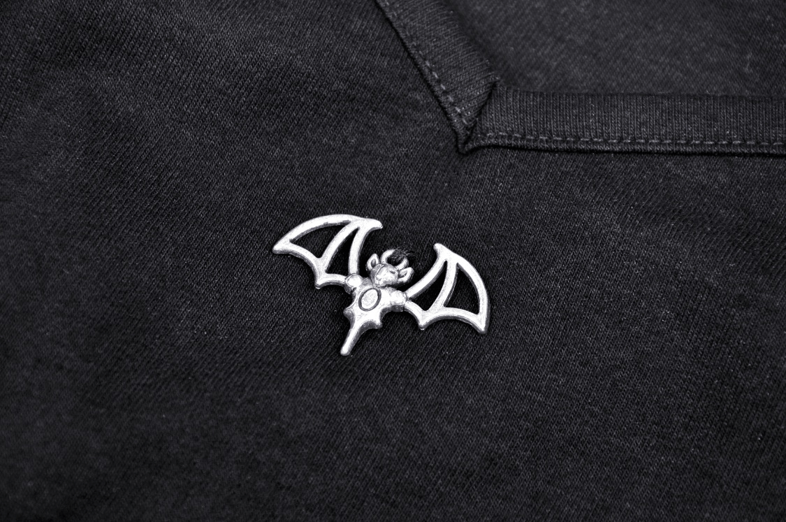 Close-up of a silver bat brooch on a black garment, adding a punk rock flair to your outfit.