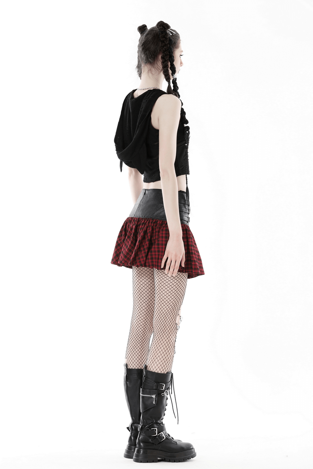Side view of a model in a punk rock black lace-up crop top, plaid skirt, and fishnet tights, showcasing edgy style.