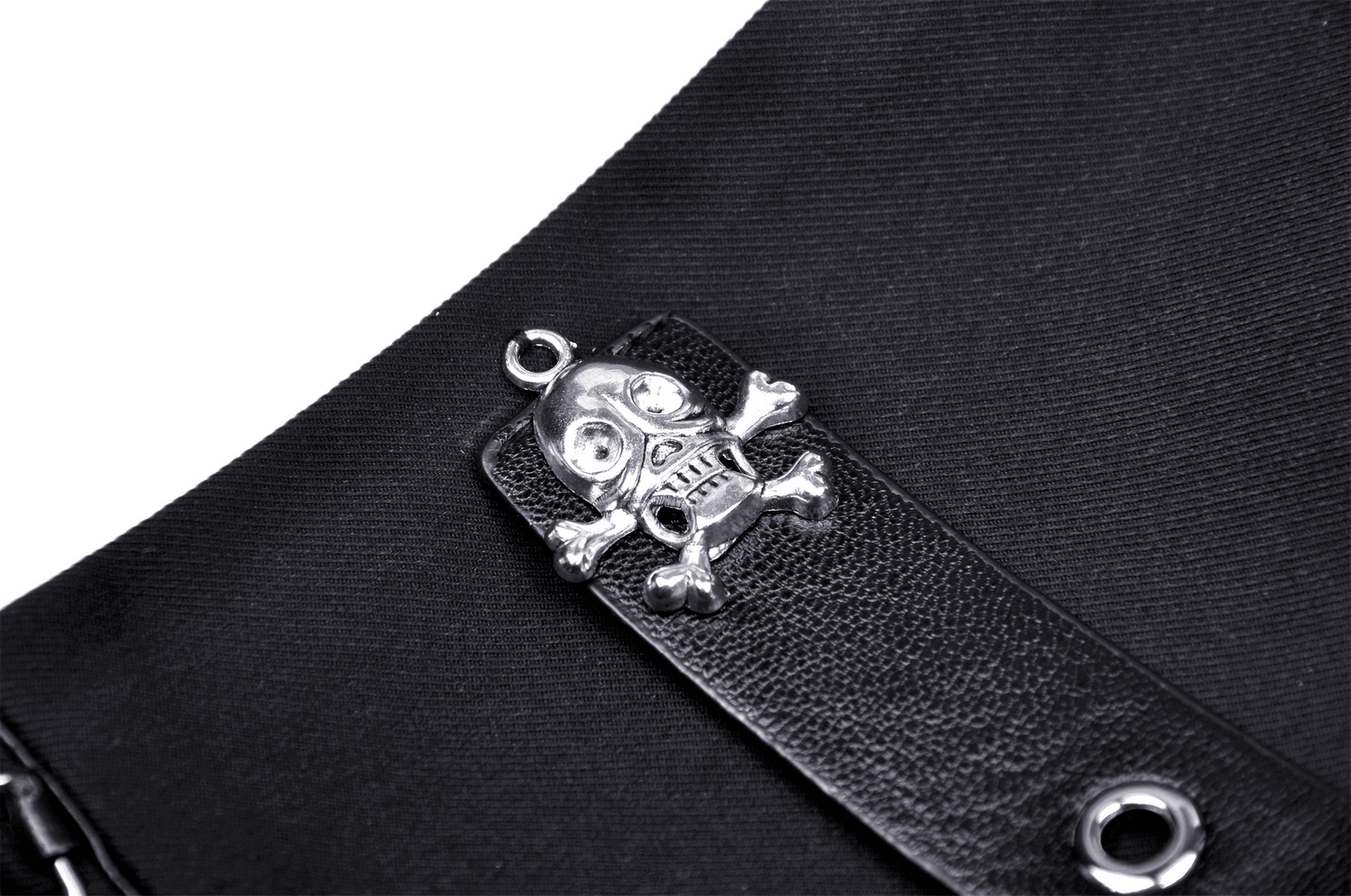 Close-up of punk rock mini skirt with silver skull and crossbones charm detail on black fabric.