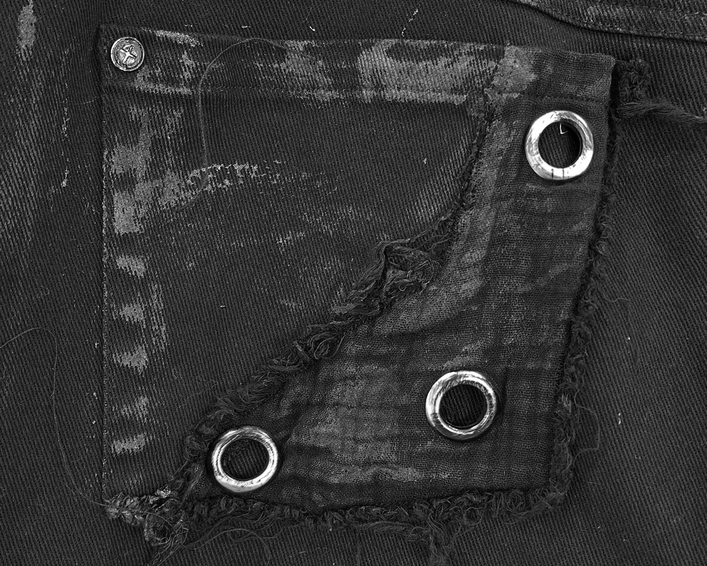Close-up of a distressed black fabric pocket with silver eyelets, highlighting punk rock design details.