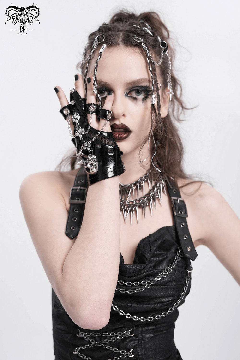 Gothic fashion model wearing punk skull studded half-finger gloves with chains, edgy black outfit, and striking makeup.