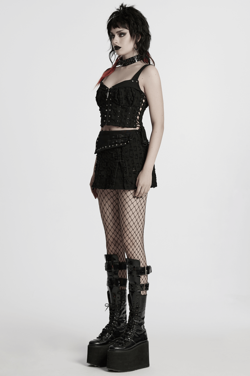 Stylish punk model in studded black denim top with adjustable drawstrings and fishnet tights, showcasing edgy fashion.